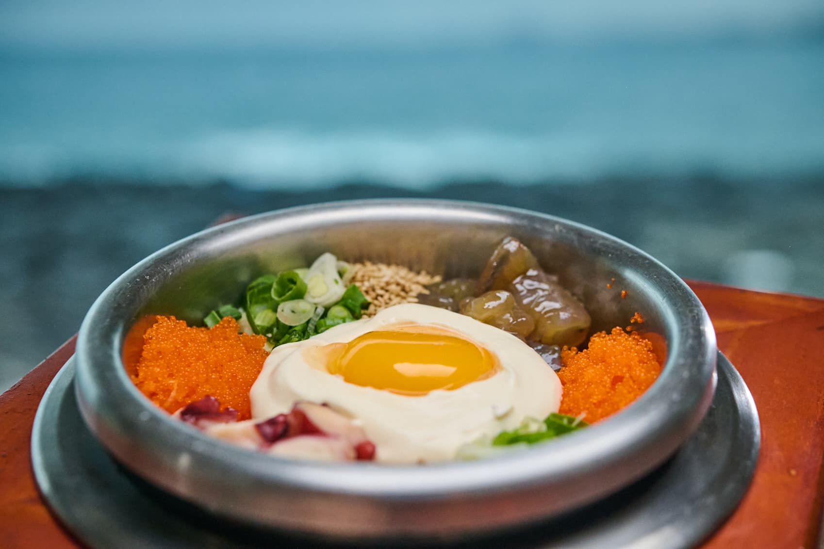 문어와 날치알, 달걀노른자를 올린 솥밥 뒤로 흐릿하게 보이는 바다